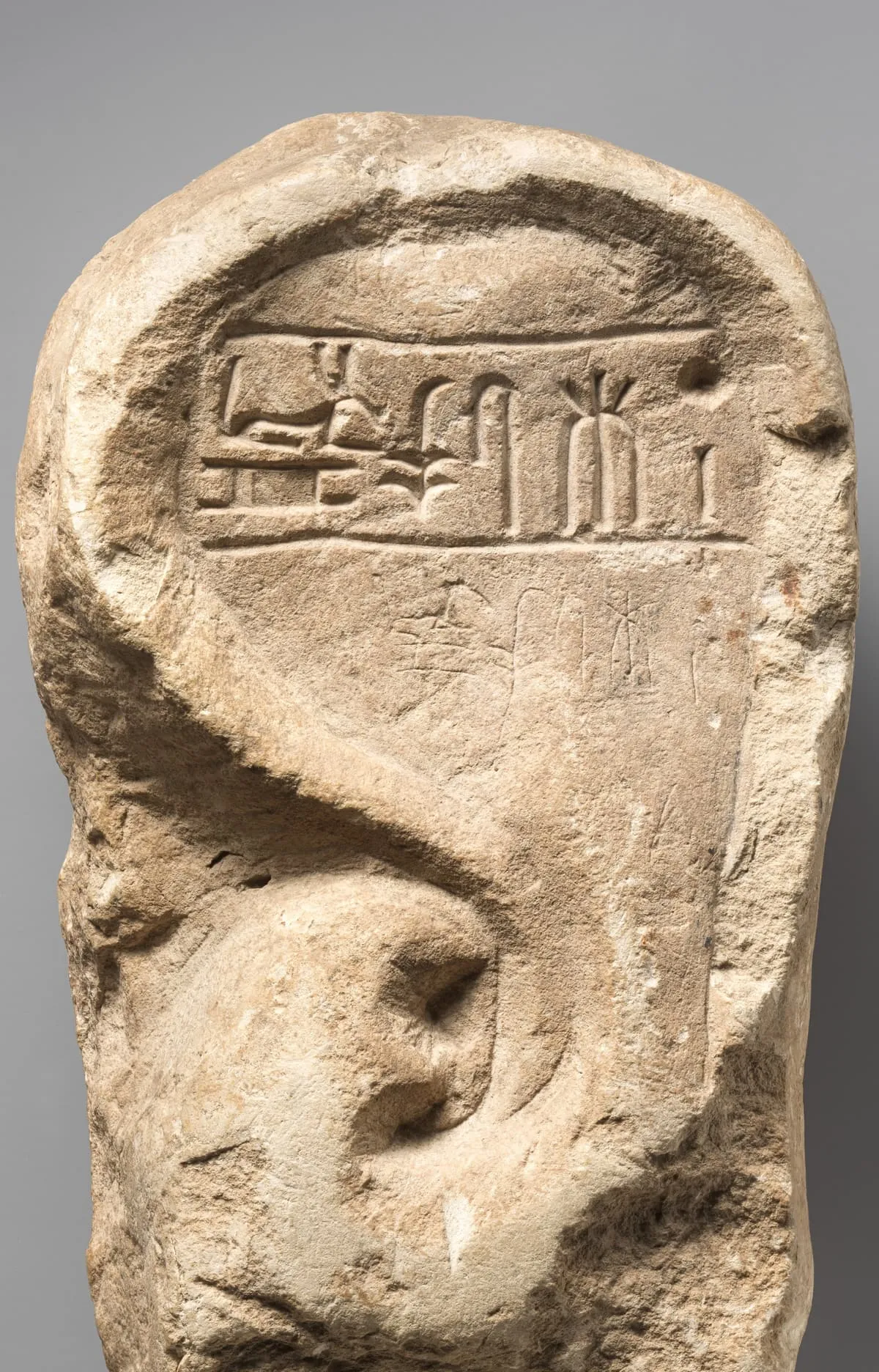 Ein grob zugehauener, hochkant stehender Kalksteinblock vor grauem Verlauf. In die Vorderseite ist oben ein flaches, oben gerundetes Feld eingetieft; darin steht eine Zeile Hieroglyphen, links davon ein sitzender Mensch vor einem niedrigen Tisch. Darunter ist in die Steinfläche ein großes menschliches Ohr eingearbeitet, mit deutlich ausgeführter Muschel und Gehörgang; sein Umriss hebt sich flach vom Grund ab. Die Ränder des Blocks sind unregelmäßig gebrochen, die Oberfläche hell, feinkörnig und stellenweise dunkel verfärbt.
