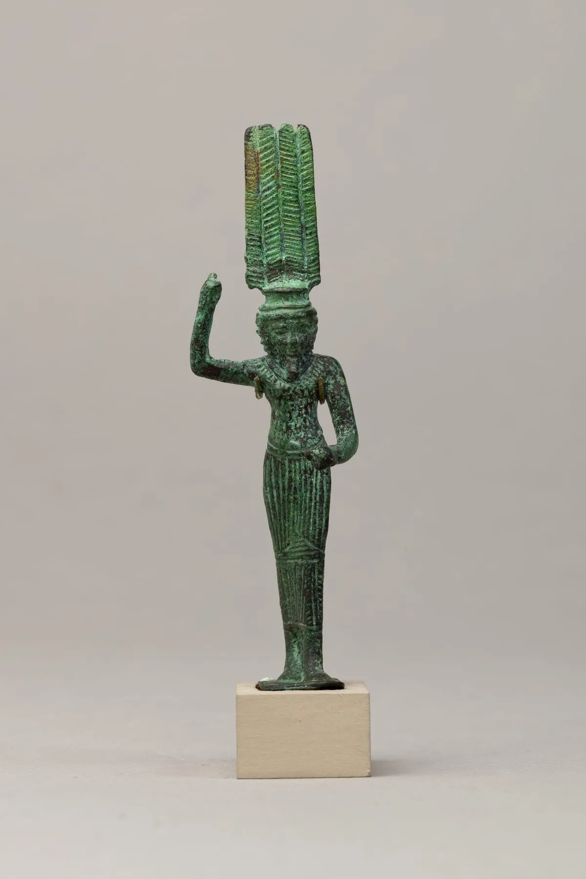 Stehende Bronzefigur mit grüner Patina auf einer Standplatte, ein Bein vorgesetzt. Der Mann trägt ein langes, fein senkrecht geripptes Gewand und einen breiten Halskragen. Ein Arm ist angewinkelt erhoben, die Hand zur leeren Faust geschlossen; der andere ist vor dem Bauch angewinkelt. Auf dem Kopf sitzt auf niedrigem Untersatz eine Krone aus vier hohen Federn mit fischgrätartiger Gliederung.